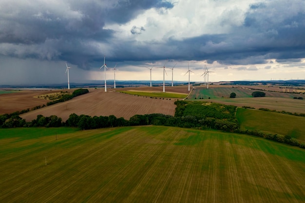 Drone vlucht op grote hoogte over een groot veld met veel draaiende windturbines De windturbines werpen een lange schaduw omdat de zon ondergaat Op de achtergrond bij stormlucht