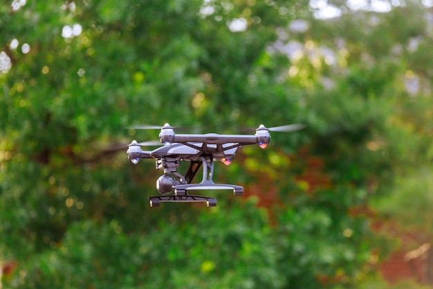 Drone with professional cinema camera flying over summer park.