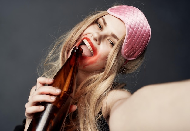 Dronken blond meisje met een flesje bier gebaren met haar handen en een helder make-up verslavingsmodel