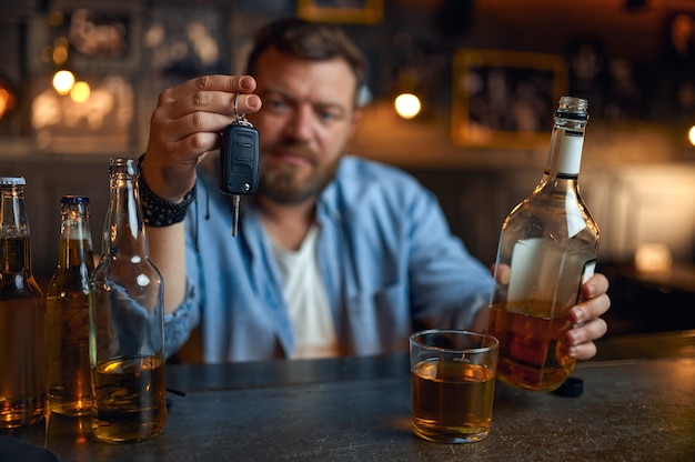 Dronken man met autosleutel zit aan de balie in de bar. Een mannelijke persoon rust in de pub, menselijke emoties en vrijetijdsbesteding. Een redelijke handeling, weigert te rijden onder invloed van alcohol