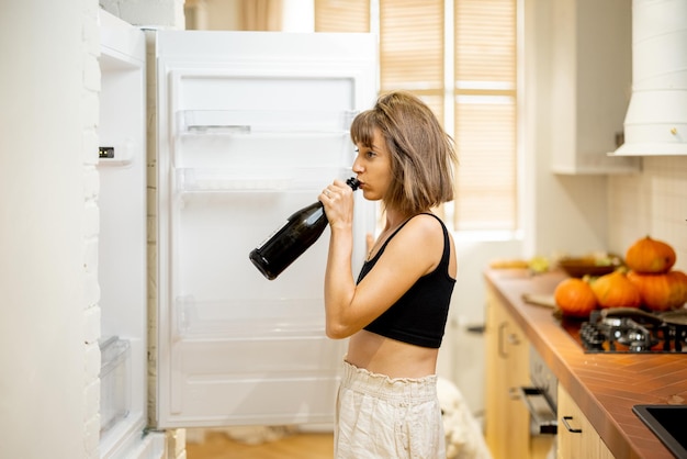 Dronken vrouw drinkt thuis wat alcohol in de buurt van koelkast