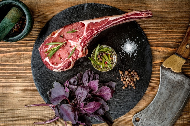 Droog verouderde rauwe tomahawk-biefstuk met ingrediënten voor het grillen op houten achtergrond. Bovenaanzicht. Ruimte kopiëren. Stilleven. plat leggen