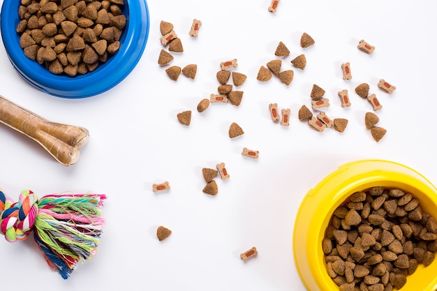 Droog voedsel voor huisdieren in kom en speelgoed voor honden op witte achtergrond bovenaanzicht