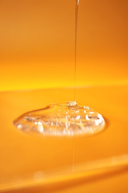 Photo a drop of body gel or shampoo pouring from above on a yellow saturated background