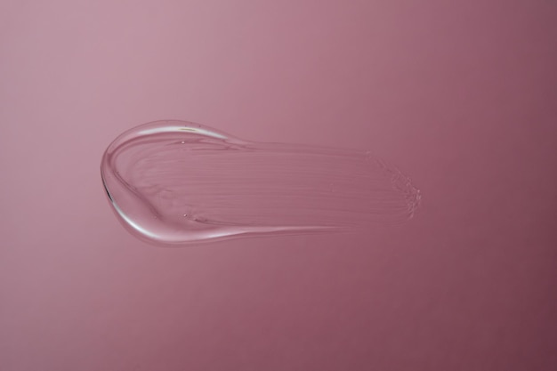 Drop of cosmetic transparent gel on a pink background The texture of the serum heir gel or hyaluronic booster