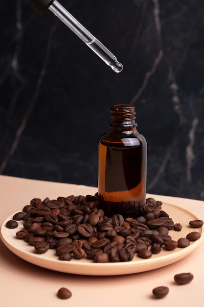 Drop falls from the pipette to cosmetic oil bottle on a beige table with coffee beans on black background