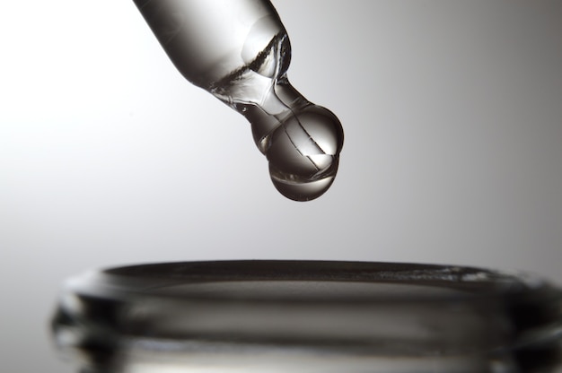 A drop falls from a pipette into a cosmetic bottle on a gray gradient background. close-up.