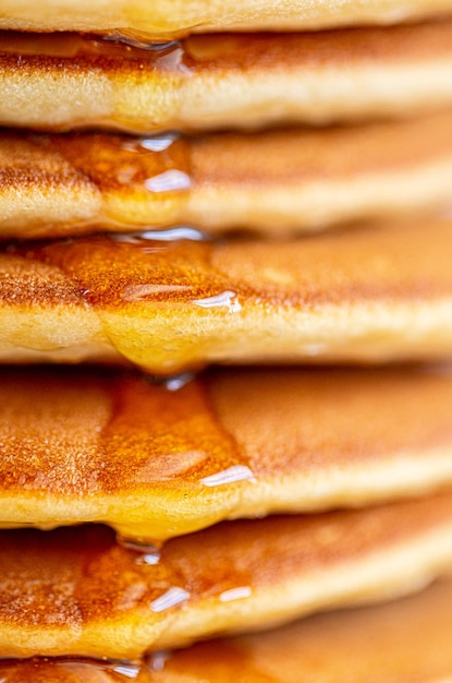 A drop of honey spreads over the pancake. pancakes with syrup macro shot. syrup pours on a pancake