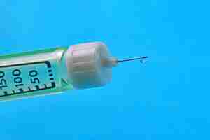 Photo a drop of medicine at the end of a syringe needle with dosage divisions closeup on a blue background vaccination of the population