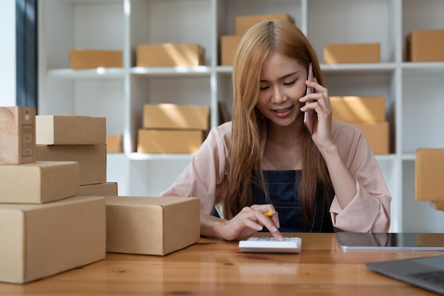 Drop shipping proprietario dell'azienda che parla sul telefono cellulare e prende l'ordine imprenditrice che lavora in ufficio a casa confermando l'ordine sul telefono