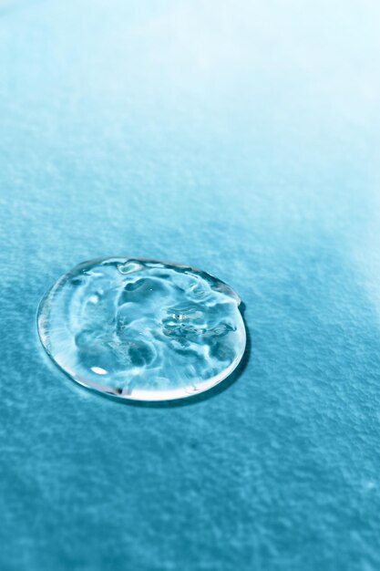 Drop of transparent cosmetic product on textured colored background closeup