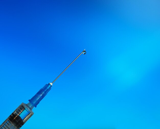 Drop of transparent vaccine on the tip of the needle syringe, blue background, a horizontal image with a soft focus, a wide banner, a place for text