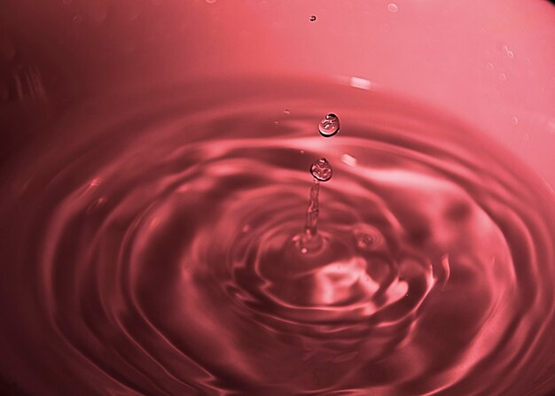 Photo drop of water on white bowl red tones bluish waves