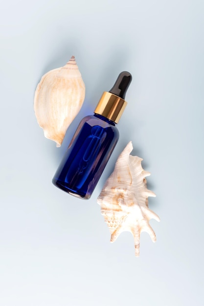 Dropper blue glass cosmetic bottle mock up and seashells on blue background Eco friendly care organic product for skin care Beauty treatment spa concept Copy space