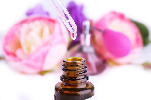 Dropper bottle of perfume with flowers on light background