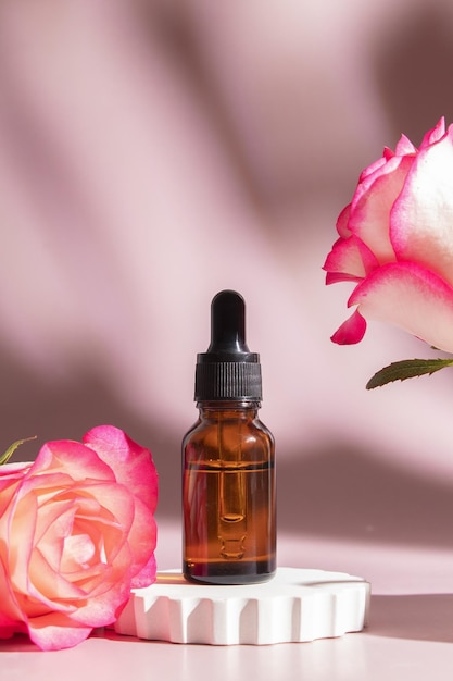 Dropper bottle with serum on a podium on pink background with rose