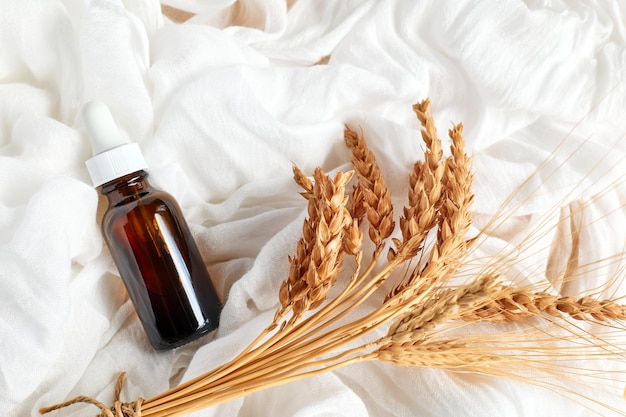 Dropper bottle with wheat extract near wheat ears on white clothe.