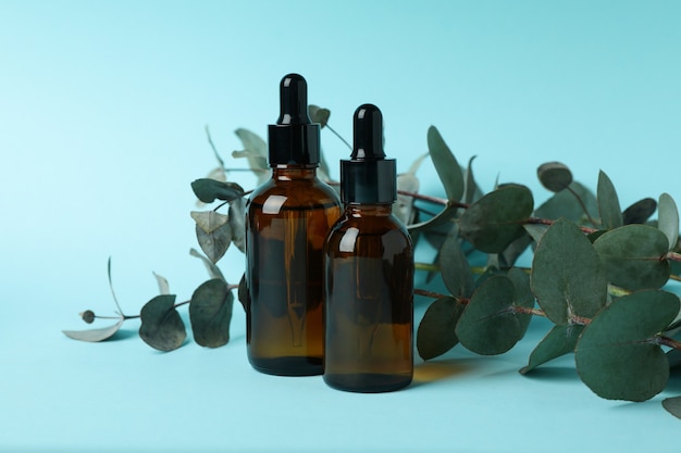 Dropper bottles of oil and eucalyptus twigs on blue background