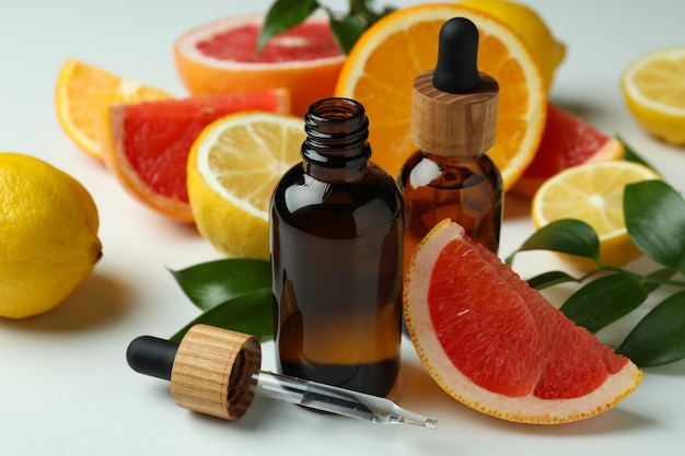 Dropper bottles with oil and different citrus on white table