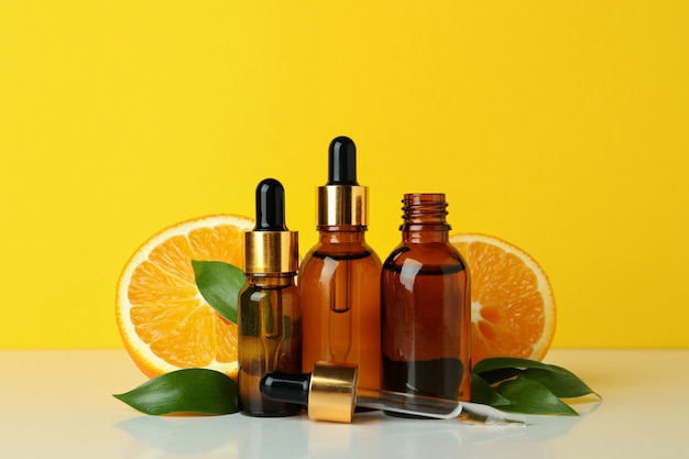 Bottiglie contagocce con olio e arance su sfondo giallo