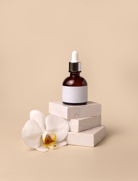 Dropper glass bottle on stone near white orchid flowers on light yellow Cosmetic Mockup