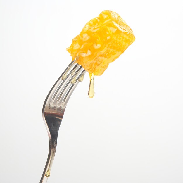 テーブルフォークにワックスハチミツから新鮮なハチミツが滴り落ちる。ビタミン栄養とミツバチ製品