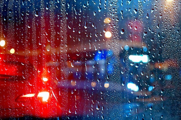 drops on glass auto road rain autumn night / abstract autumn background in the city, auto traffic, romantic trip by car