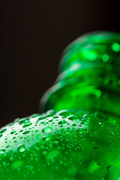 Капли на зеленой бутылке с водой крупным планом