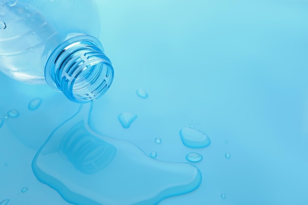 Photo drops of spilled water and plastic bottle on light blue background closeup