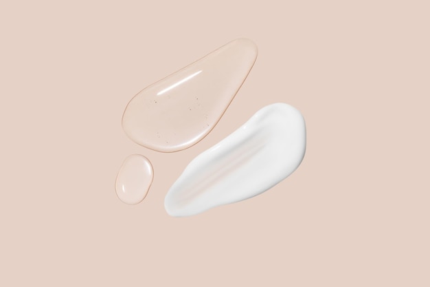 Drops of transparent gel and a dab of white cosmetic cream On a beige background