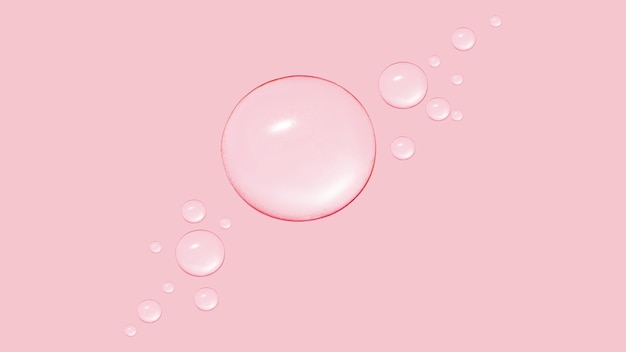 ピンクの背景にさまざまなサイズの透明なジェルまたは水の滴