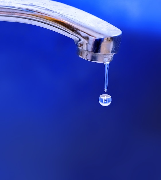 Foto gocce d'acqua che gocciolano dal primo piano della gru di ferro su priorità bassa blu. concetto di uso razionale delle risorse naturali