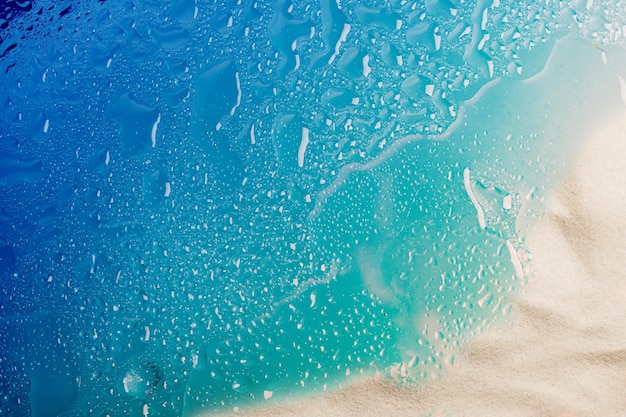 Drops of water and snowwhite beach sand on blue glass Abstract summer background