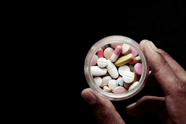 Drug abuse concept with many pills on hand against black background