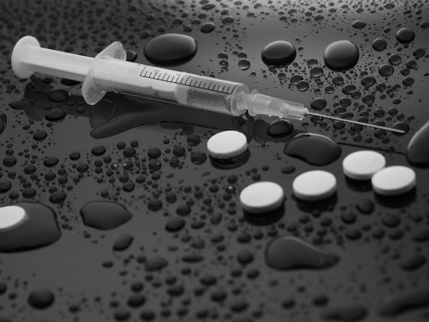 Drug concept, addiction. Syringe and pills on dark background