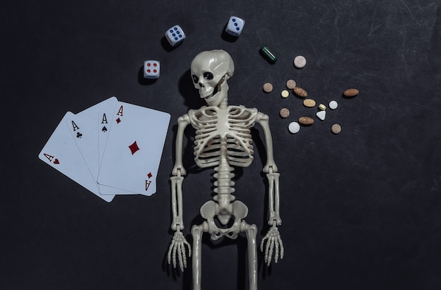 Drug and gambling addiction. Skeleton, four aces, dice, pills on black background. 