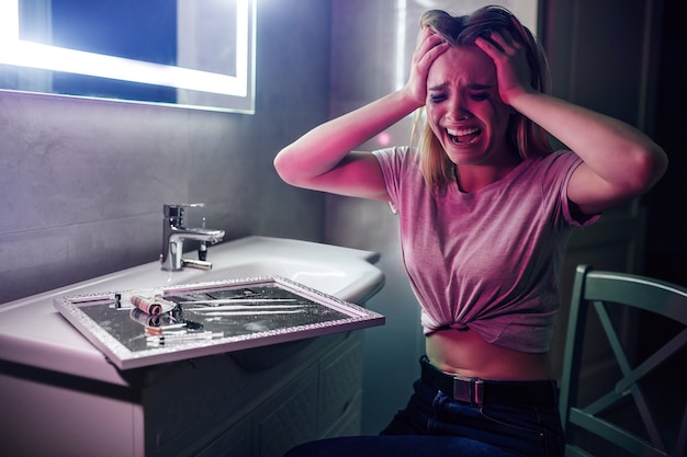 Drug obsession and pain. Drug addict holds hands on her hand and is going crazy near drugs. Drug addicted woman with smeared makeup screaming in dark night club's toilet. Find strength to fight