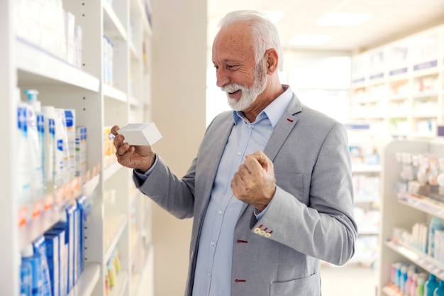 Drug shopping. An old man in good physical and mental shape reads the declaration on the medicine. He is happy because he found the package that the pharmacist recommended to him
