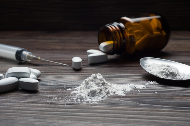 Drugs set - powder and pills and syringe on wooden background (selective focus)