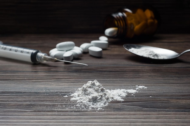 Drugs set - powder and pills and syringe on wooden background (selective focus)