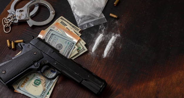 Photo drugs smuggling and trafficking handcuffs pistol money and cocaine on wooden table background