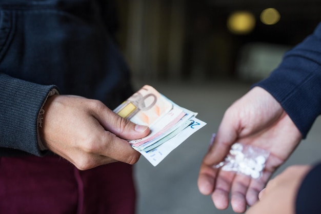 Drugshandel, misdaad, verslaving en verkoopconcept - close-up van verslaafde met geld die dosis koopt van dealer op straat