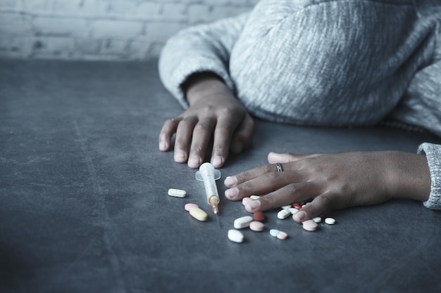 drugsverslaving concept met hand met pillen en spuit op de vloer.