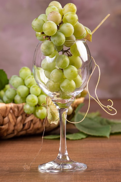 Druiven, trossen groene druiven geplaatst samen met een rieten mand en een kristallen beker op een houten oppervlak, selectieve focus.
