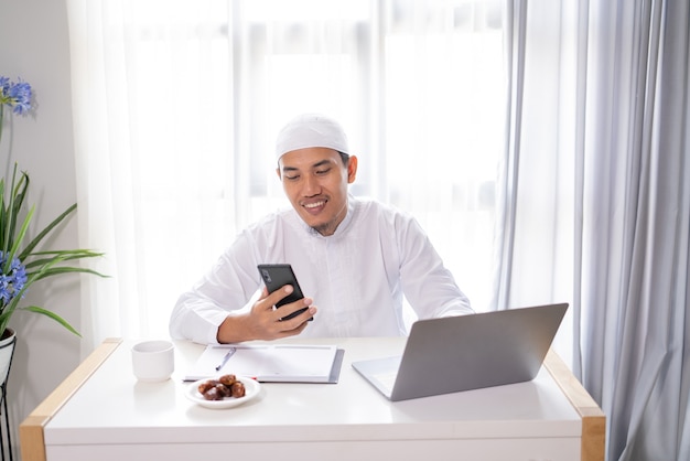 Drukke aziatische moslimzakenman die zijn smartphone en laptop gebruiken die vanuit huis werken