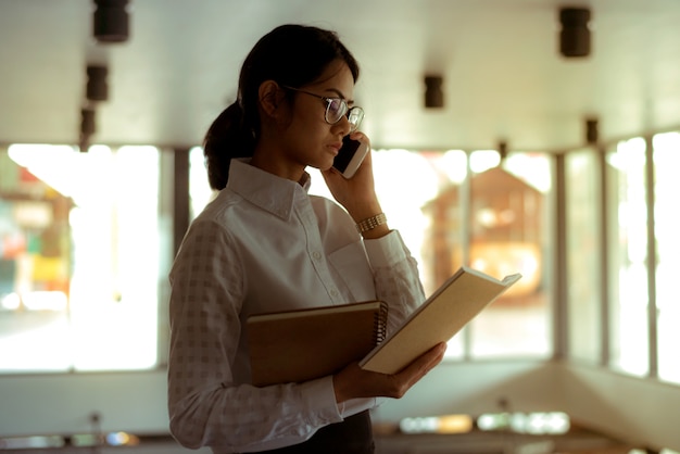 Drukke Aziatische onderneemster die smartphone gebruiken die over bedrijfsbespreking spreken terwijl het lezen van financieel rapport