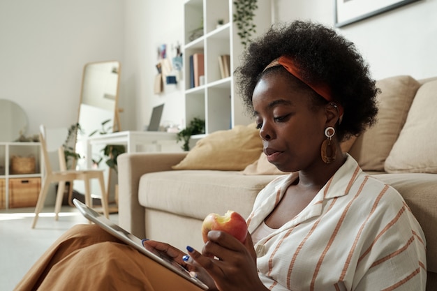 Drukke jonge Afrikaanse freelancer met appel scrollen in tablet