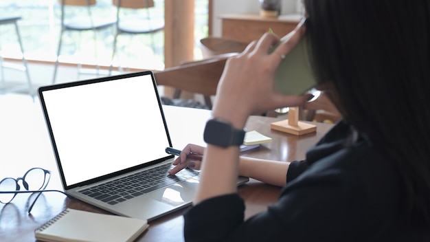 Drukke jonge vrouw die een gesprek voert op de mobiele telefoon en aan een computerlaptop werkt