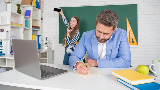 Drukke schoolleraar in de klas met selectieve focus van kind dat selfie maakt op blackboard