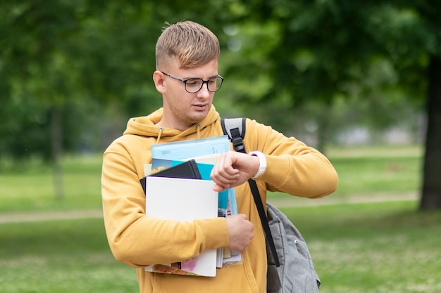 Drukke universiteitsstudent die met boeken zijn polshorloge bekijkt